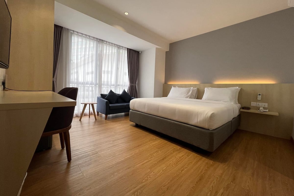 A modern hotel room with a large bed, a desk, a chair, and a sofa.