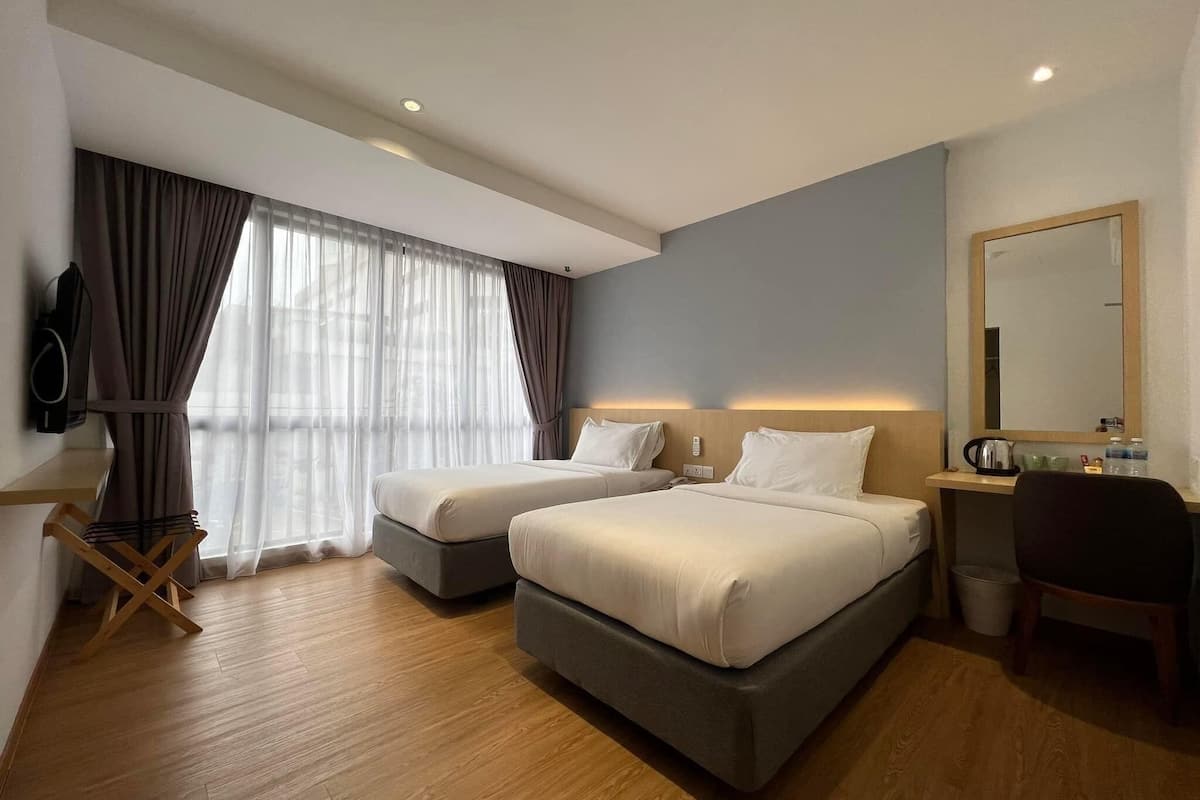 A hotel room with two beds, a desk, a chair, a TV, and a large window with curtains.