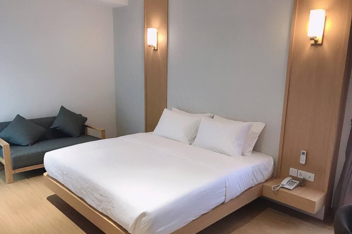 A hotel room with a large bed, a bedside table with a phone, and a couch.