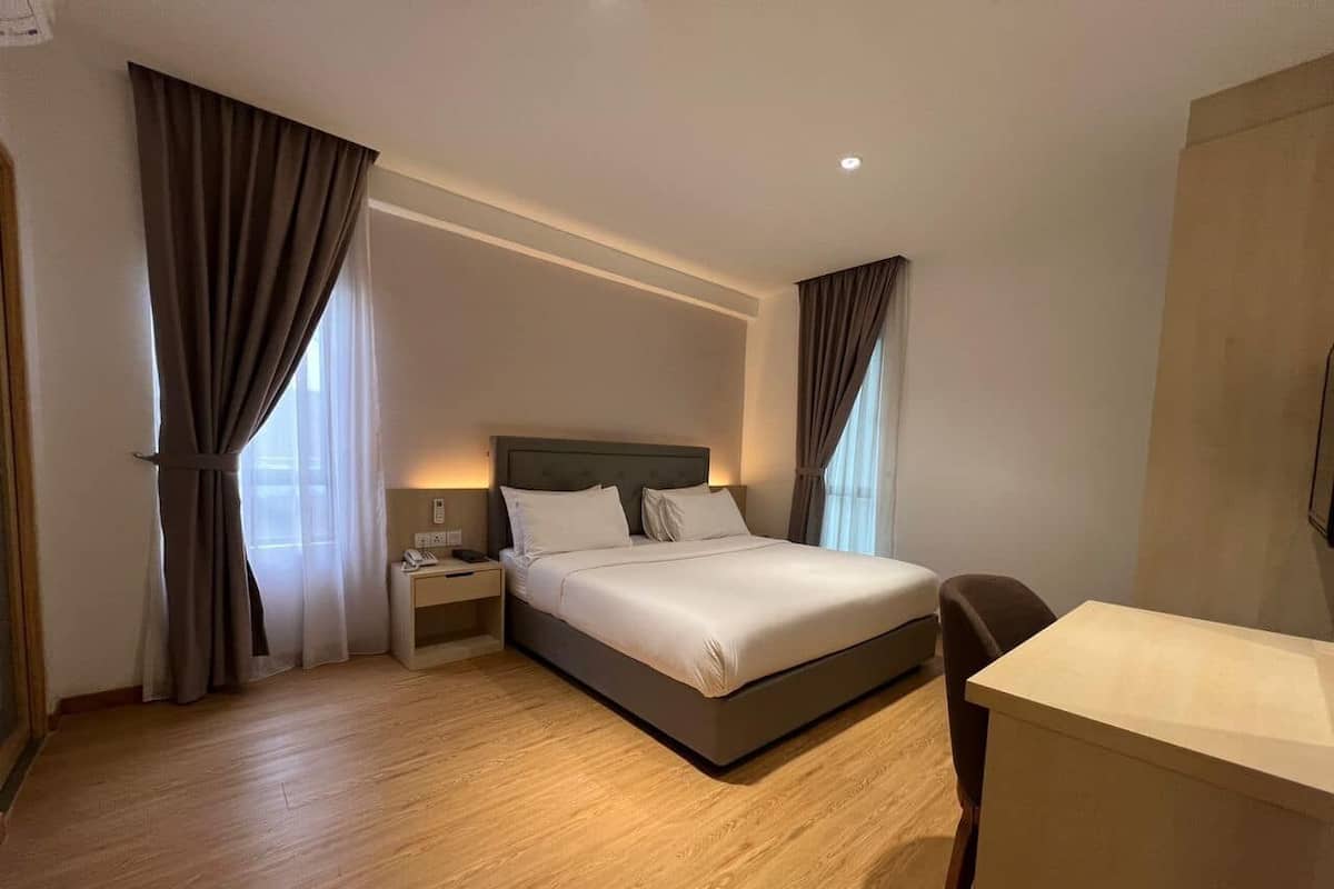 A hotel room with a bed, bedside table, lamp, and a desk.