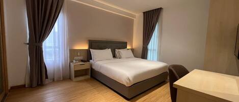 A hotel room with a bed, bedside table, lamp, and a desk.