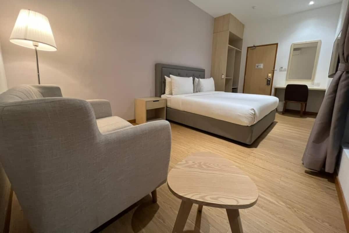 A modern hotel room with a bed, a sofa, a small table, a lamp, a wardrobe, and a mirror.
