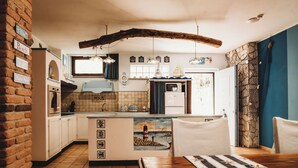 Una cocina con armarios blancos, una isla de madera, luces colgantes y una pared de piedra.
