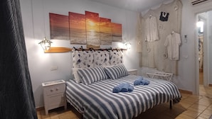 Un dormitorio con cama, mesita de noche, lámpara de pared, un cuadro y una puerta que da a otra habitación.