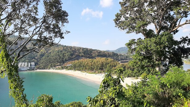 Eine Küstenlandschaft mit Strand, üppiger Vegetation und einem weit entfernten Gebäudekomplex.