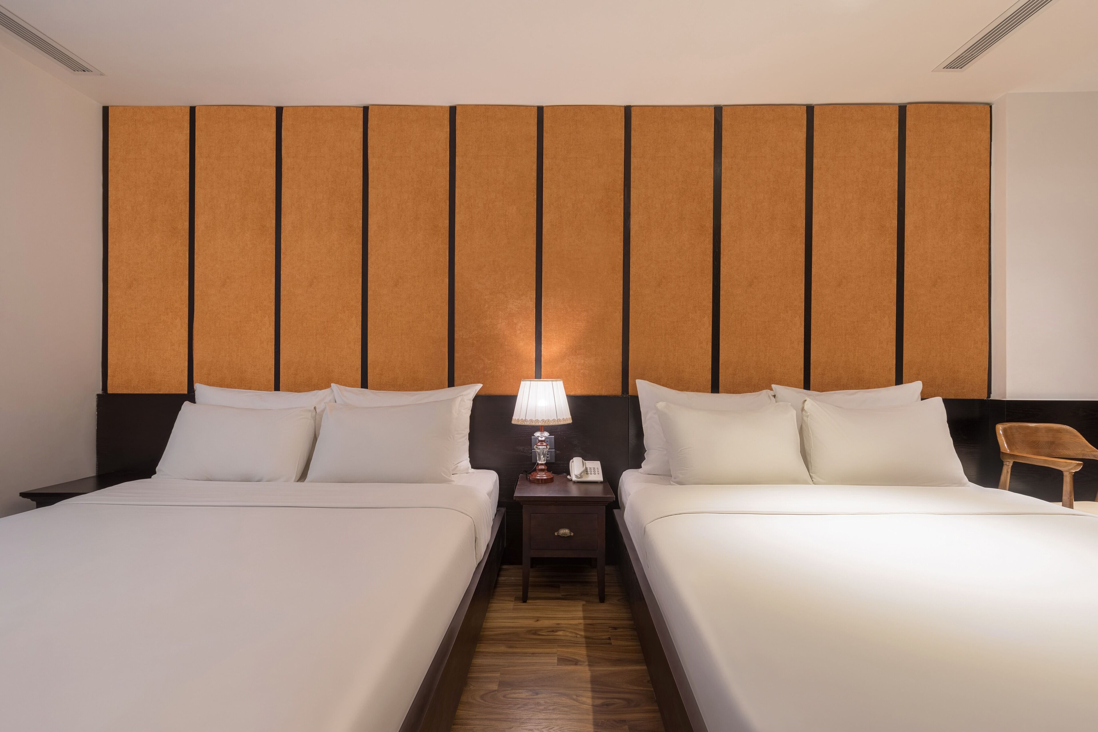 A hotel room with two beds, a nightstand with a lamp, and a wooden headboard.