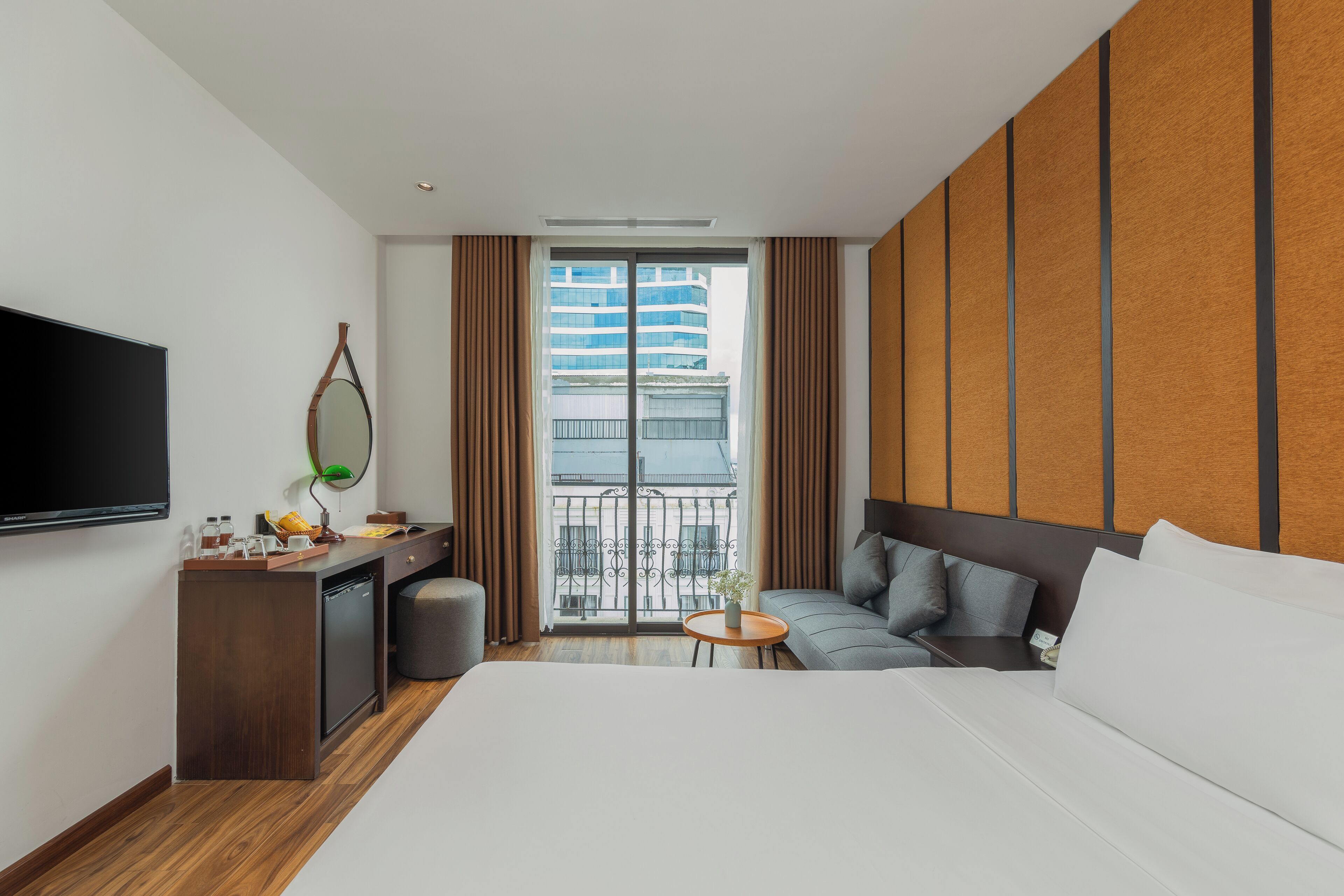 A hotel room with a bed, a desk with a flat-screen TV, a small table, and a sofa.