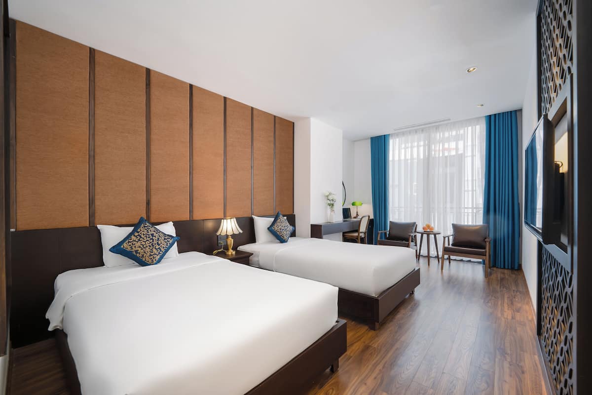 A hotel room with two beds, a desk, a chair, and a TV.
