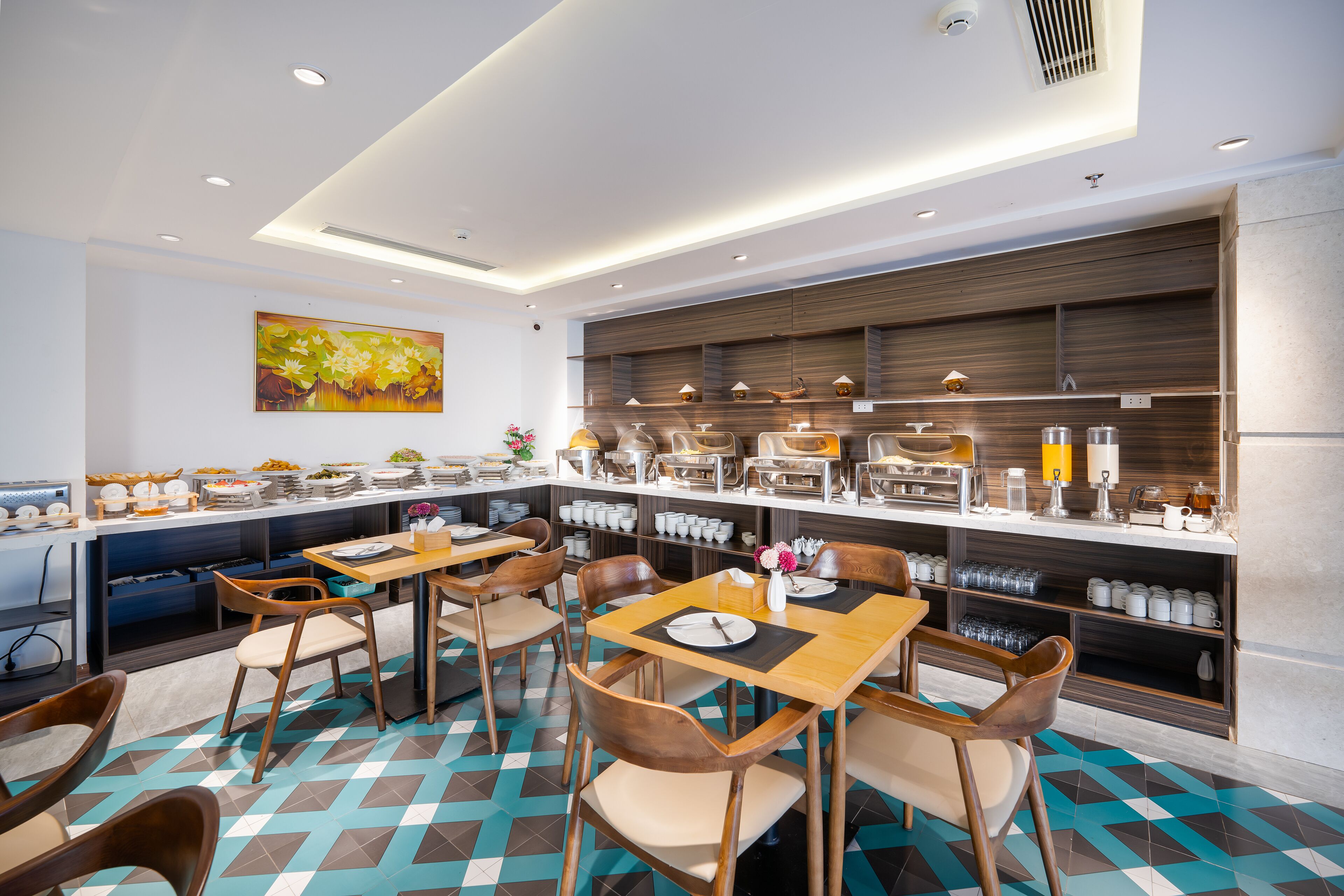 A modern dining area with wooden tables and chairs, a buffet counter with various food items, and a decorative wall painting.