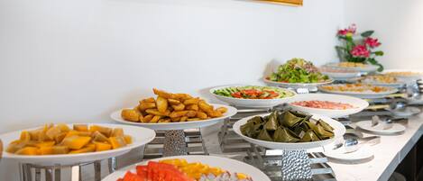 Un bufé con diversos platos, entre ellos frutas, verduras y alimentos preparados.