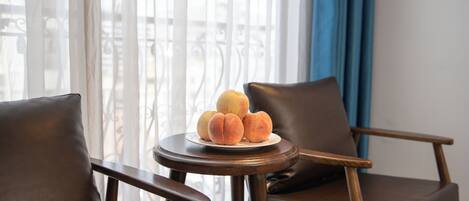 Una habitación con vistas a un balcón, una mesa redonda de madera con un plato de melocotones y dos sillones de cuero.