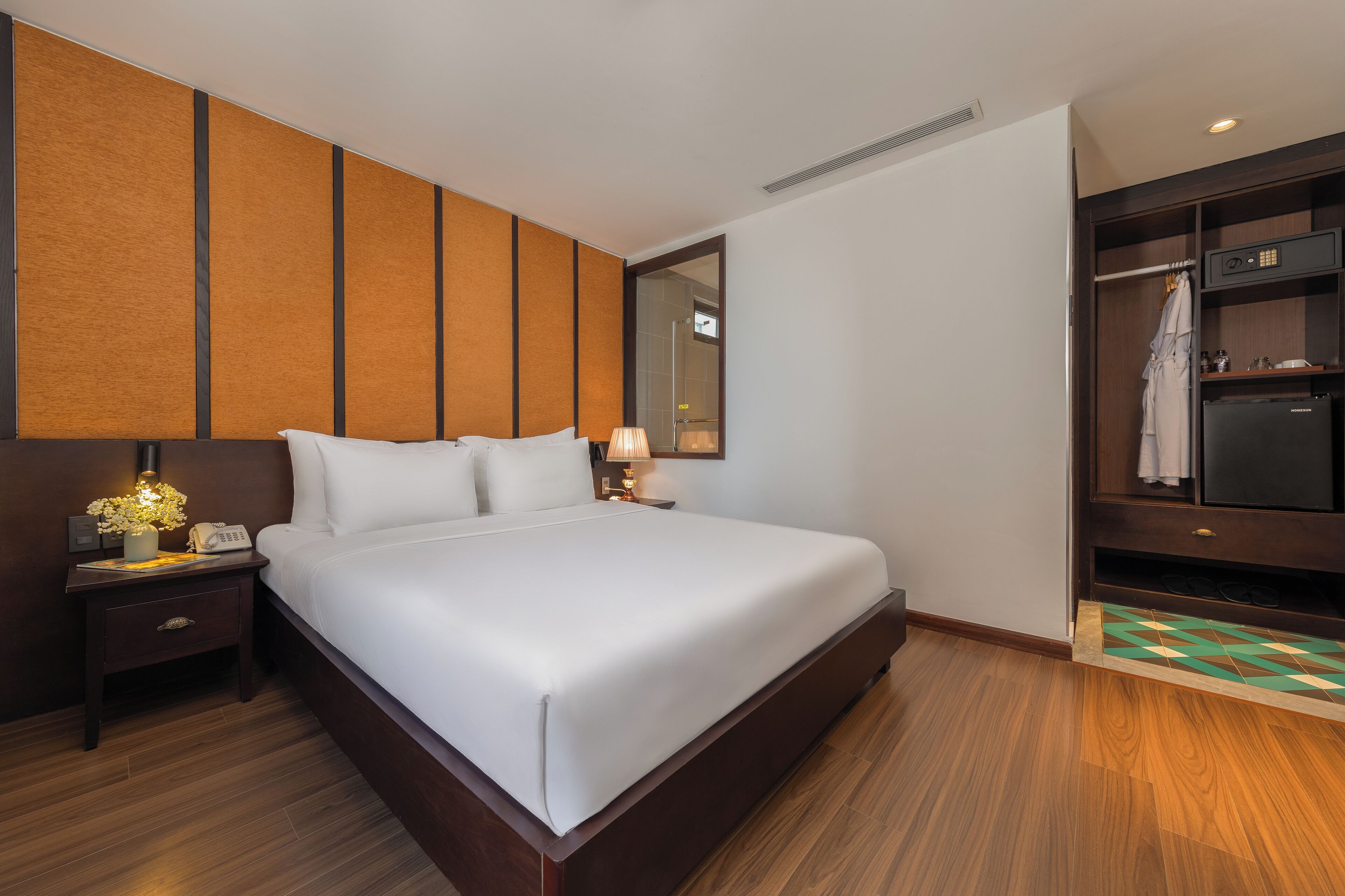 Ein Hotelzimmer mit einem großen Bett, einem Nachttisch mit Lampe, einem Kleiderschrank und einem Spiegel.