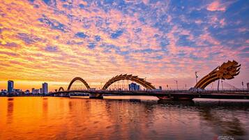 Un pont orné de sculptures en forme de dragons à chaque extrémité, enjambant une étendue d’eau, avec la silhouette d’une ville en arrière-plan.
