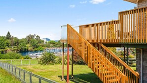 Um deck de madeira com uma escadaria que leva a um edifício, com vista para a água e vegetação.