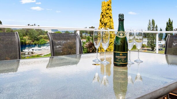 Mesa com uma garrafa de vinho Hinchinbury e três copos numa varanda com vista panorâmica.