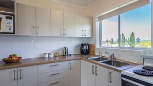 Cozinha moderna com armários brancos, bancada de madeira, forno embutido e janela com vista para árvores e edifícios.