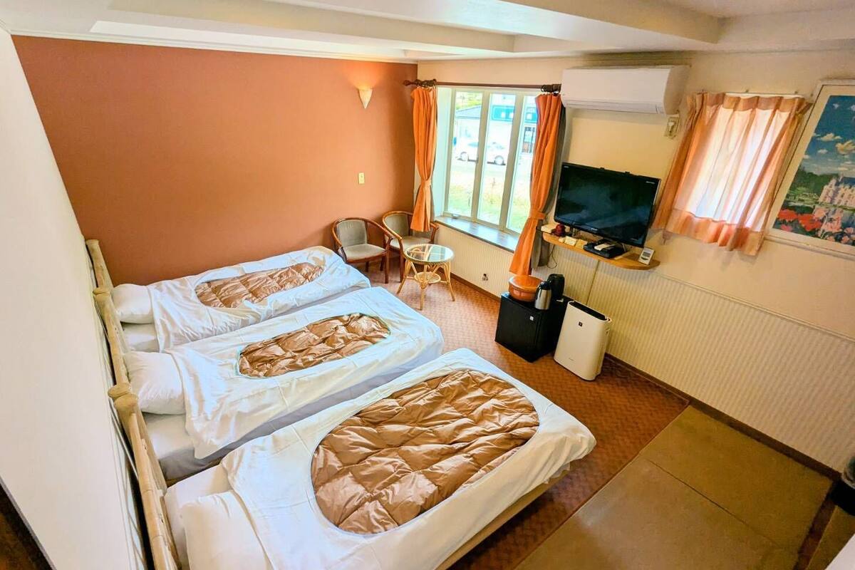 Habitació d'hotel amb dos llits, una televisió, una taula petita i una finestra amb cortines.