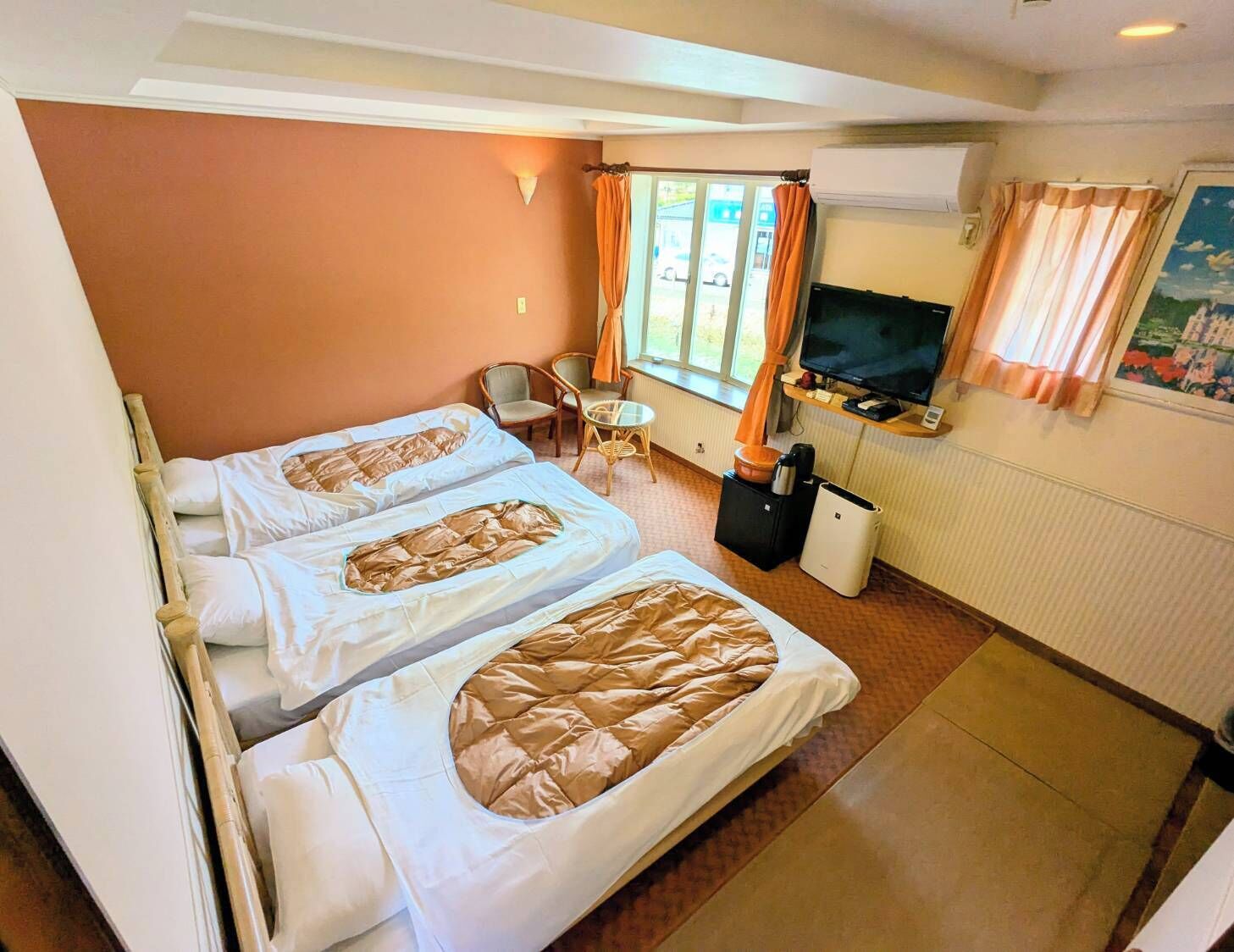 A hotel room with two beds, a TV, a small table, and a window with curtains.