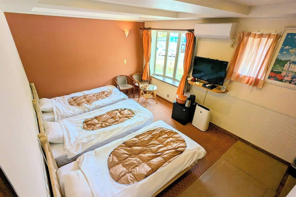 Habitació d'hotel amb dos llits, una televisió, una taula petita i una finestra amb cortines.