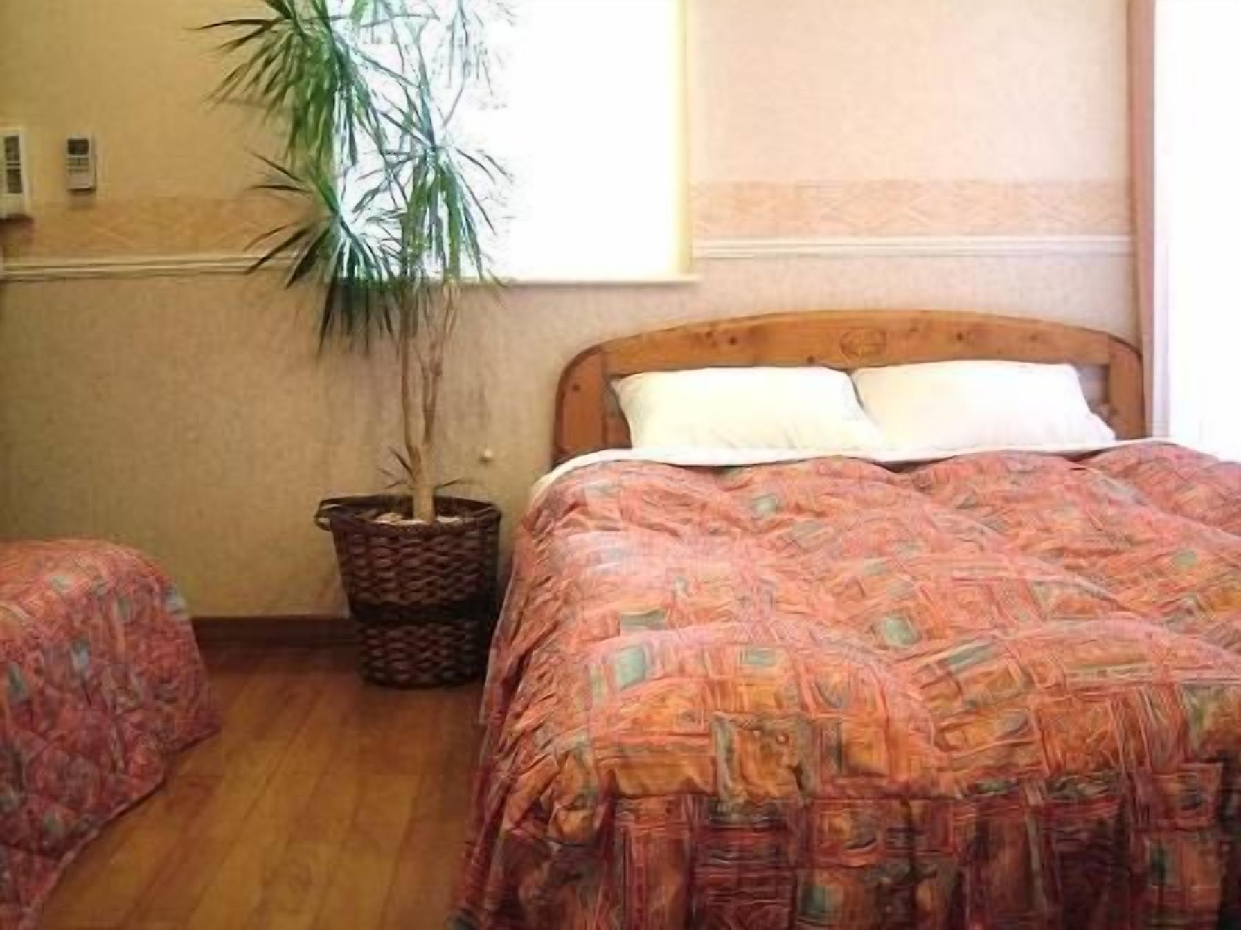 A bedroom with a wooden bed, a potted plant, and a window.