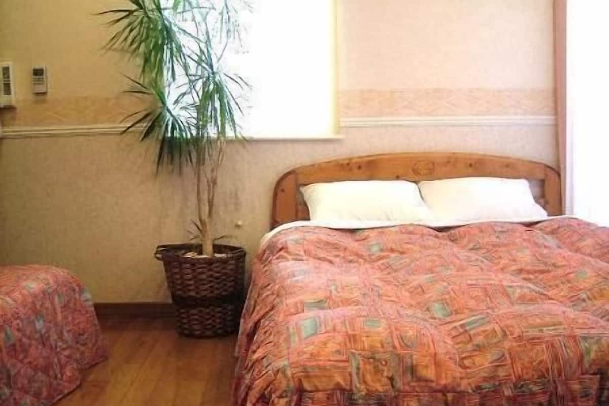 Un dormitori amb llit de fusta, una planta en test i una finestra.