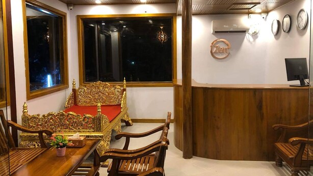Una habitación con un sofá de madera tradicional, una mesa de comedor de madera y sillas. Hay un ventanal grande, un aire acondicionado instalado en la pared y un reloj en la pared.