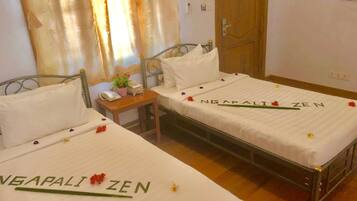 A hotel room with two beds, each bedspread has 'NEGAPALI ZEN' printed on it. There is a small table with a phone and a plant between the beds.