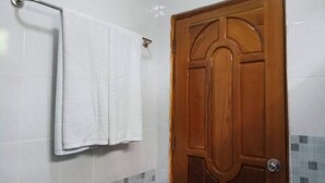 Un baño con puerta de madera, paredes de azulejos blancos y una toalla colgada en un perchero.