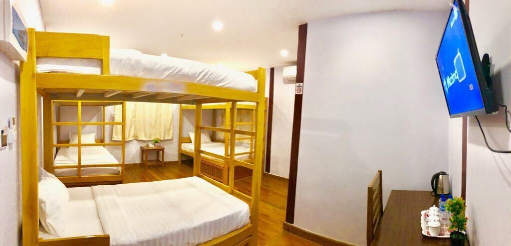 A bunk bed room with a television on the wall, a small table with a plant, and a kettle.