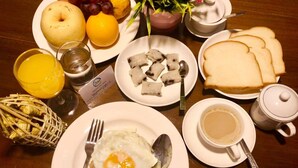Un desayuno que incluye un plato de huevo frito con arroz, un plato de dumplings, tostadas, una taza de café y una cesta de frutas con manzana, uvas y naranja.