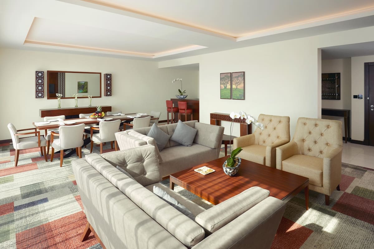 A modern living room with a sofa, armchairs, a coffee table, and a dining area with chairs and a table.