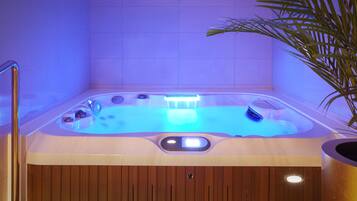 Un bain à remous avec une base en bois, un panneau de commande et une plante à proximité.