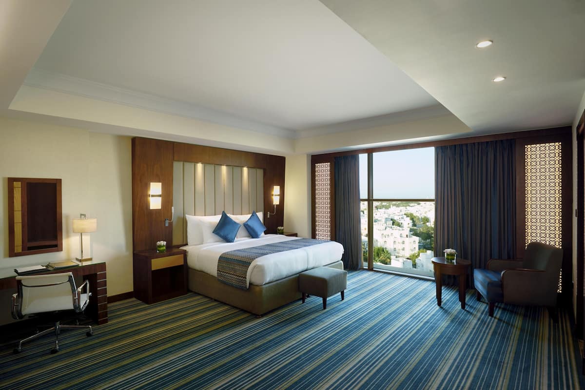 A hotel room with a large bed, a desk, a chair, and a view of the city.