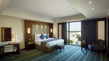 A hotel room with a large bed, a desk, a chair, and a view of the city.
