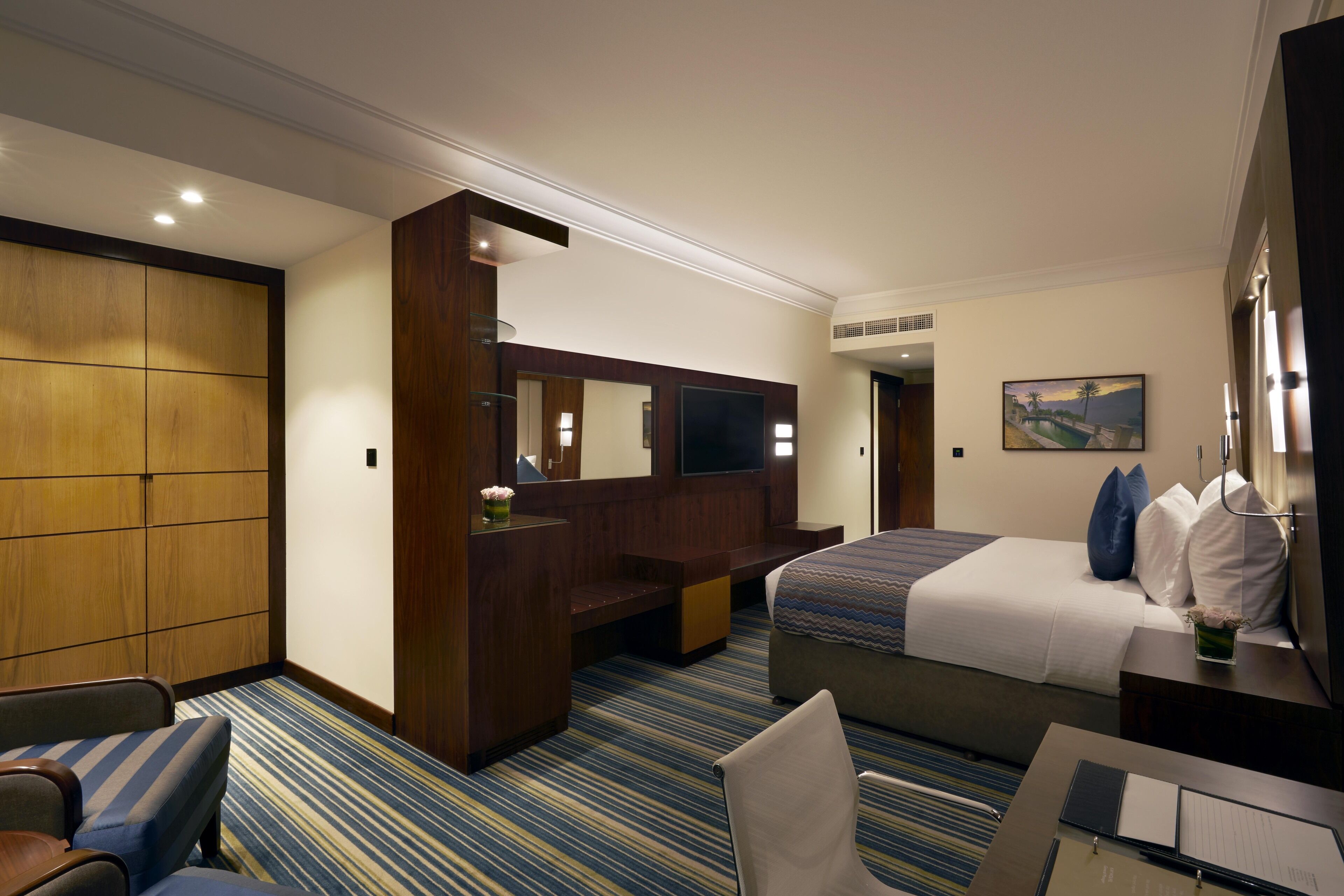 Una habitación de hotel con cama, escritorio, silla, televisor y un espejo grande.