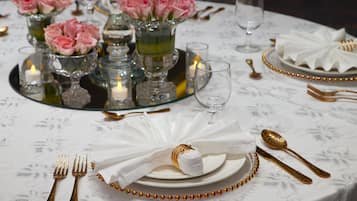 A table set with white plates, gold cutlery, and pink roses in glass vases.