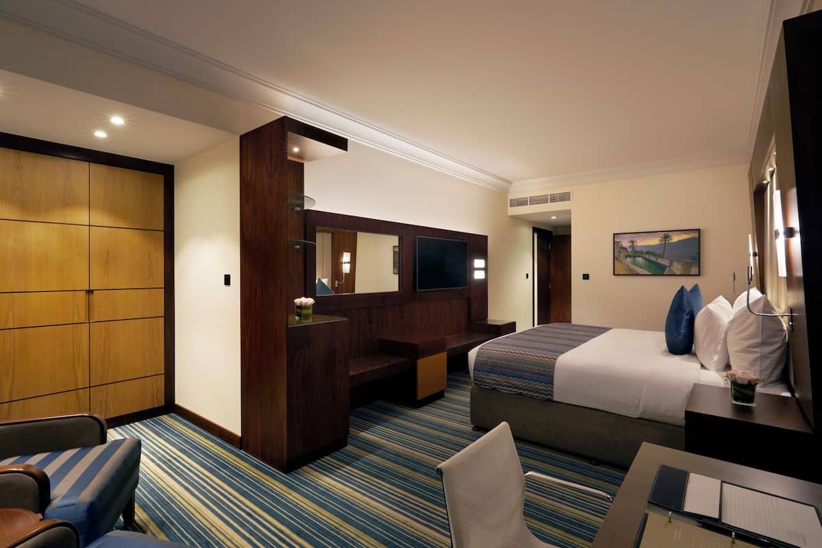 A hotel room with a bed, a desk, a chair, a TV, and a large mirror.