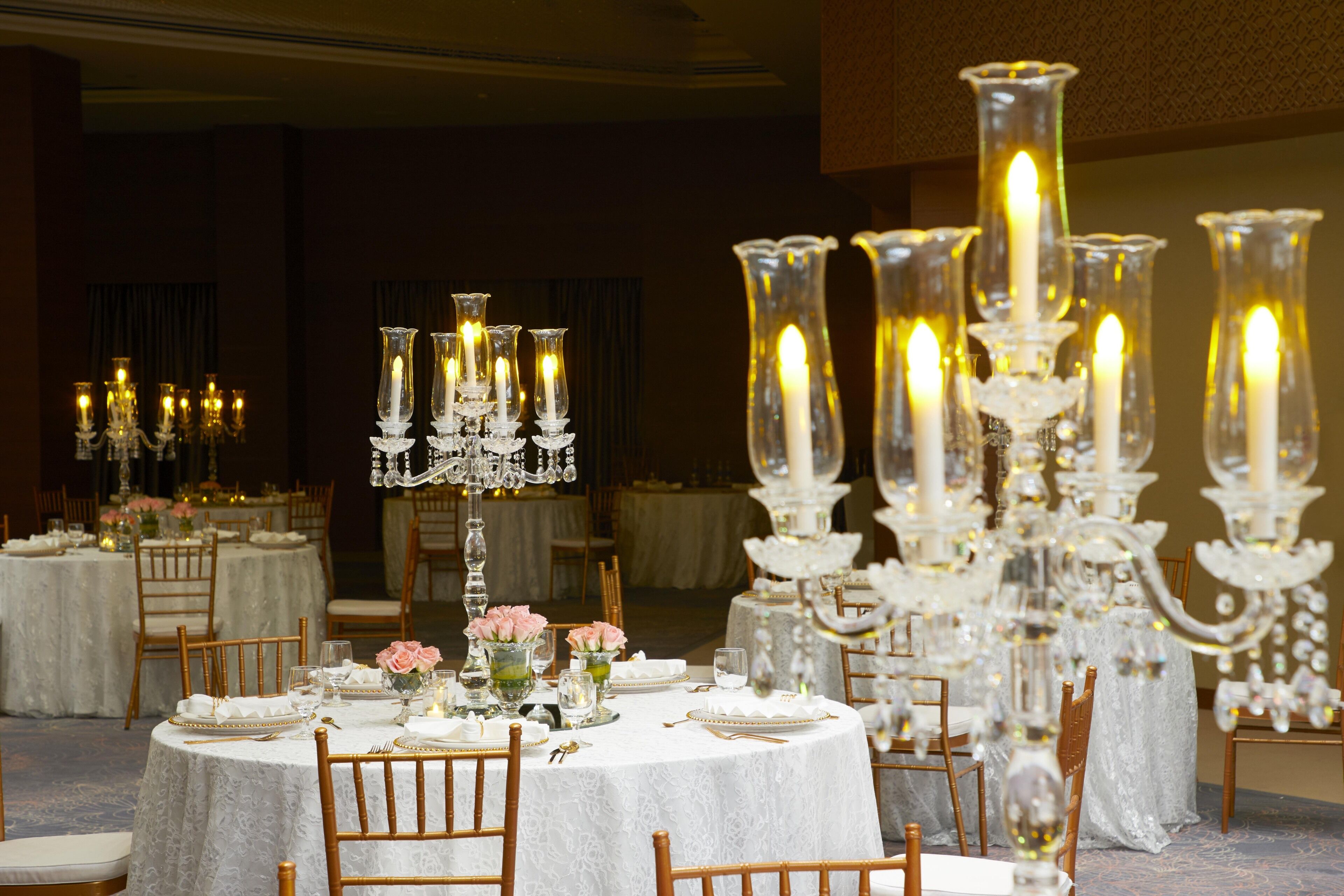 A banquet hall with round tables set for dining, adorned with white tablecloths and crystal candelabras.