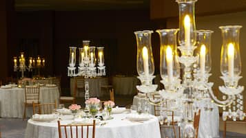 A banquet hall with round tables set for dining, adorned with white tablecloths and crystal candelabras.
