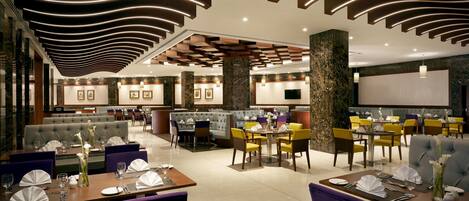 Un restaurant moderne offrant différents types de sièges, notamment des banquettes et des tables, un espace bar et un grand écran pour les présentations.