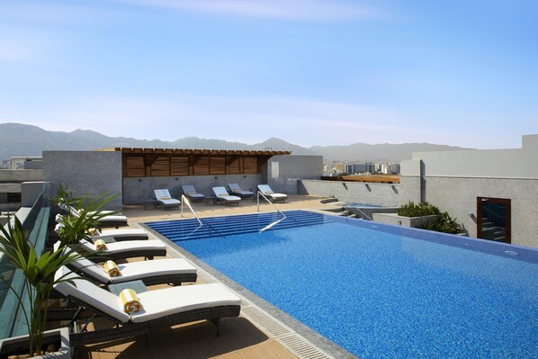 A rooftop pool area with lounge chairs and a small building with a wooden roof. - Royal Tulip Muscat (Muscat)
