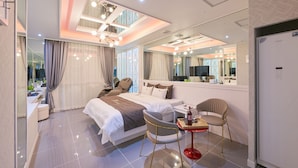 A modern hotel room with a large bed, a sitting area with a table and chairs, a mirror, and a bathroom visible through an open door. - 1Beonji Muintel (Gwangyang)