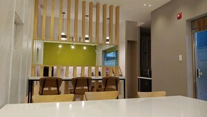 A modern dining area with a white table and chairs, a green partition, and a kitchen area visible through a glass door. - 1Beonji Muintel (Gwangyang)