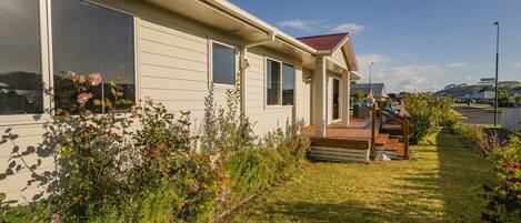 A single-story house with a front porch, a small deck, and a well-maintained garden with various plants and flowers.