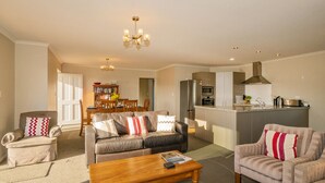 A modern living room with a sofa, armchairs, a coffee table, and a bookshelf. - Home Base - Cooks Beach Holiday Home (Cooks Beach)