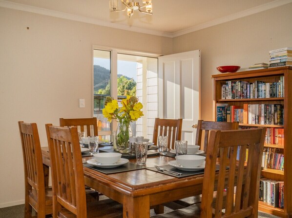 Un comedor con una mesa de madera dispuesta para cuatro personas, rodeada de sillas. A la derecha, una estantería llena de libros.