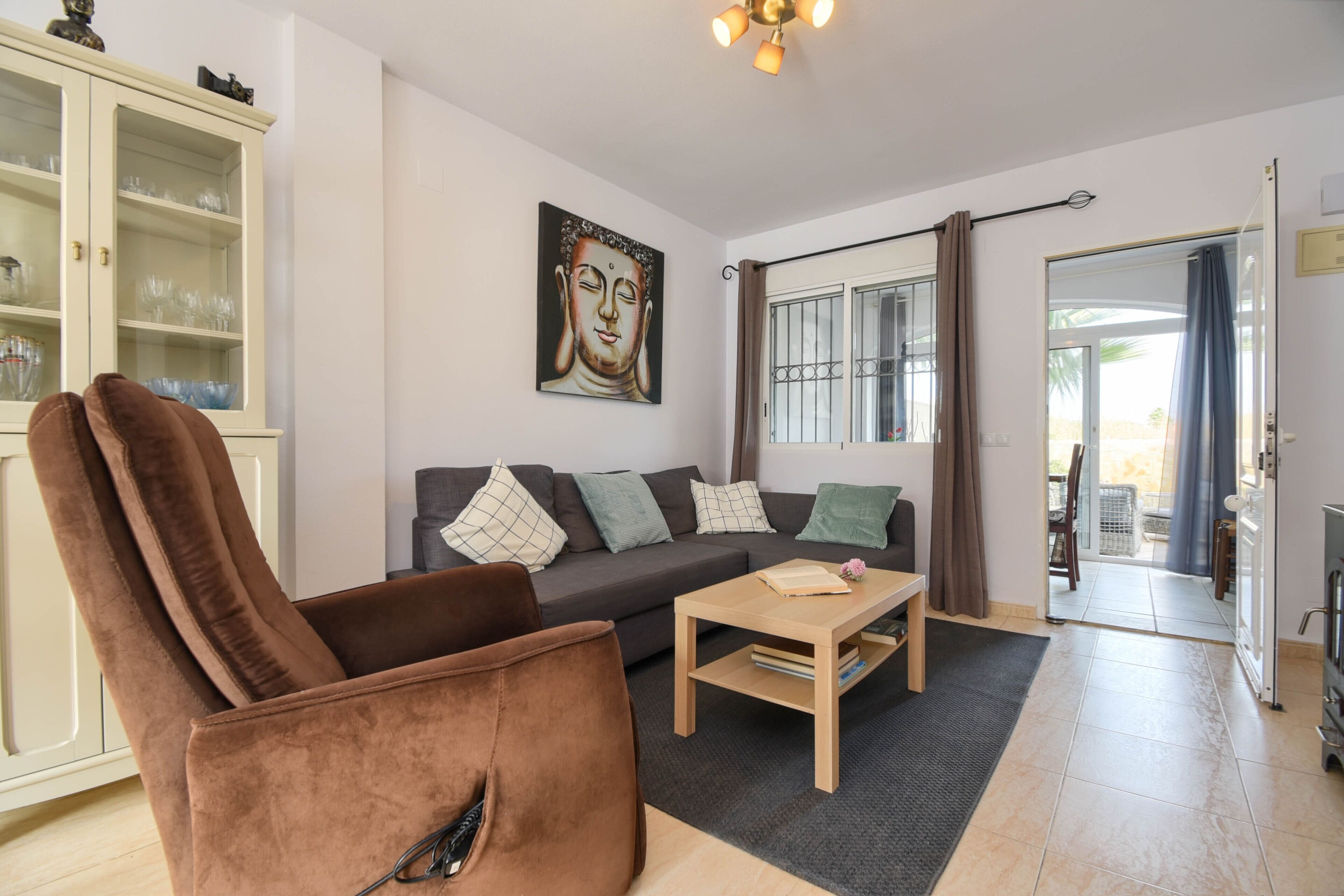 Una sala de estar con un sofá, un sillón marrón, una mesa de centro y un aparador con puertas de vidrio.
