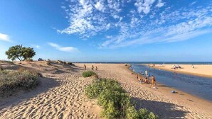 A beach with clear skies and scattered clouds, sandy terrain, and a few people in the distance.