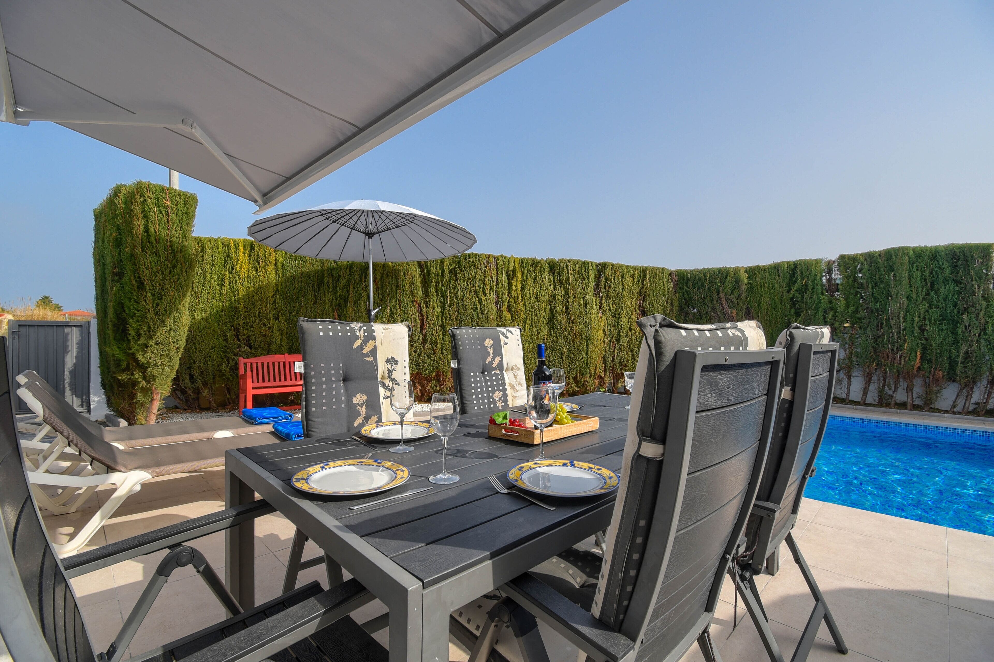 An outdoor dining area with a pool, a table set with plates and glasses, and a red chair.