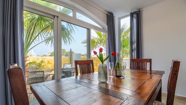 A dining table with chairs, a vase with flowers, and a bottle of wine.